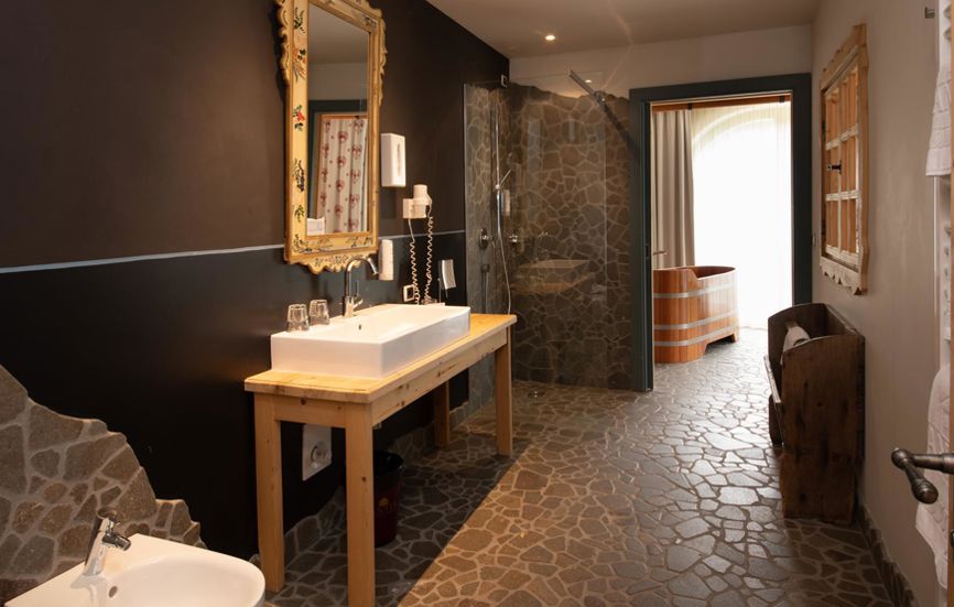 Bagno con pavimento in pietra naturale, doccia, bidet, lavandino e vasca panoramica -  Suite Lodge Jürgen