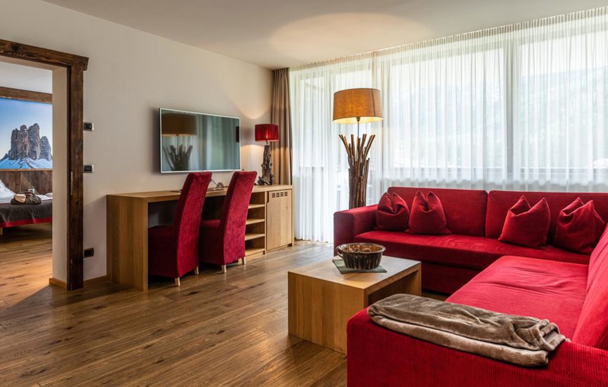 Living room with red wrap-around sofa, desk and flat screen TV - Suite Lodge Saskia
