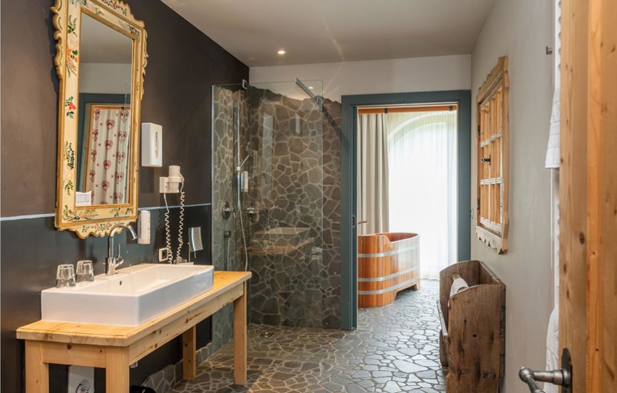 Badezimmer mit Natursteinboden, Dusche, Waschbecken und Panoramabadewanne - Suite Lodge Jürgen