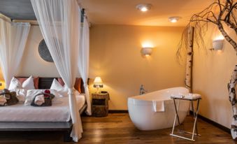 Schlafzimmer mit Doppelbett, Badewanne und Baum - Suite Lodge Stephanie