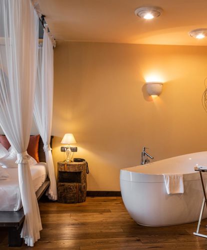 Schlafzimmer mit Doppelbett, Badewanne und Baum - Suite Lodge Stephanie