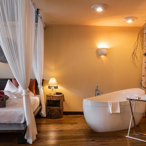 Schlafzimmer mit Doppelbett, Badewanne und Baum - Suite Lodge Stephanie