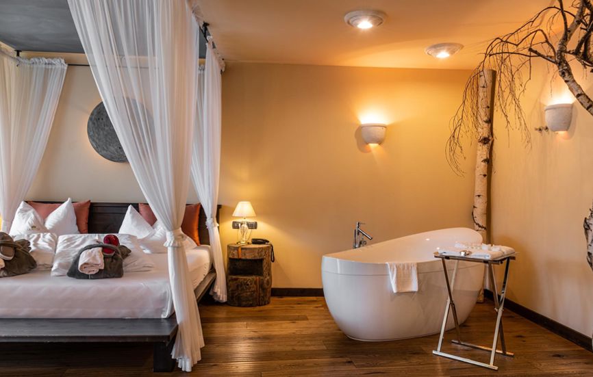 Schlafzimmer mit Doppelbett, Badewanne und Baum - Suite Lodge Stephanie