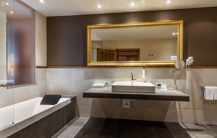 Modern bathroom with bathtub, sink and a mirror in a golden frame - Double room Landro Lodge